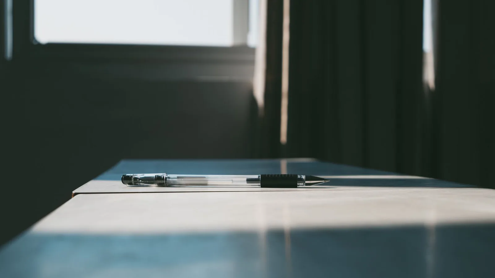 Un stylo posé seul sur un bureau clair baigné par la lumière d'une fenêtre